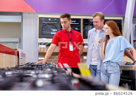 couple choosing hob in household appliances store, talking with consultant 86024526