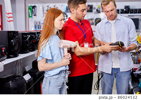 cute female standing with hair dryer in store while husband talking with consultant 86024532