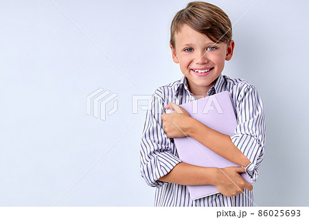 Portrait of happy kid holding book, hugging it, stand isolated over white background studio. 86025693