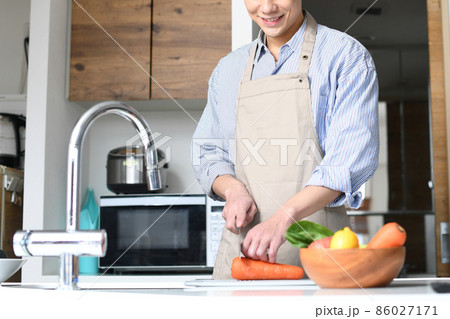 キッチンで料理をするエプロン姿の若い黒髪の男性 86027171