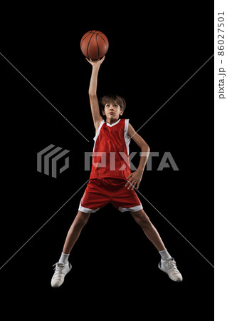 Full-length studio shot of basketball player in motion, jumping and throwing ball isolated over black background 86027501