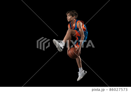 Full-length studio shot of young boy, teenager, basketball player in motion, training isolated over black background Full-length studio shot of young boy, teenager, basketball player in motion, training isolated over black background 86027573
