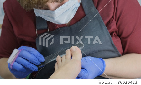 master makes a pedicure to a client in a beauty salon, using a foot nail file, peeling the skin of master makes a pedicure to a client in a beauty salon, using a foot nail file, peeling the skin of 86029423