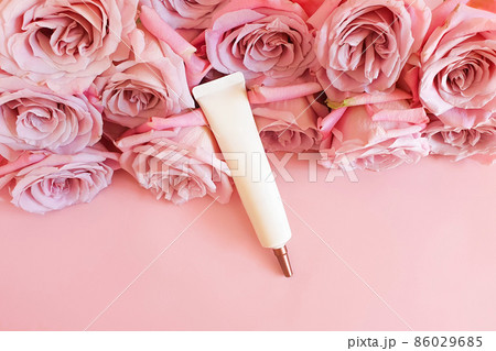 White ivory squeeze cosmetic tube with long nozzle and bronze screw cap and pink roses on pink background. Bottle for branding - cream, gel, skincare, moisturizer, mockup. Top front view, flat lay. 86029685