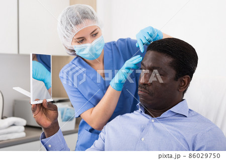 Cosmetologist examining male client face before procedure in clinic Cosmetologist examining male client face before procedure in clinic 86029750