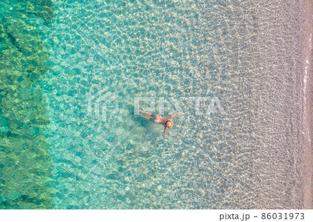Top view. Young beautiful naked woman in a hat swimming in sea water on sand beach. Drone, copter photo. Summer vacation. View from above. 86031973