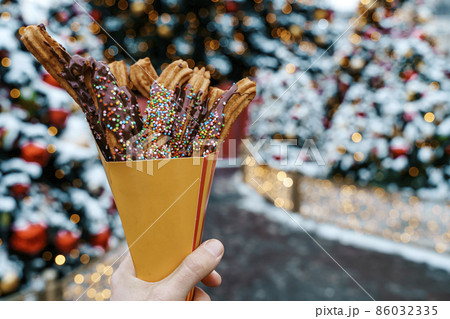 Churros waffles in a hand on the winter snow market. Churros Mexican street food dessert. Fast food sweets, Christmas fair cookies 86032335