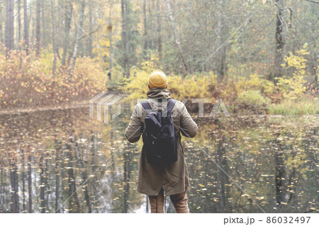Traveler in the woods. A man with a backpack walks and trips on a track in a beautiful autumn forest and admires the lake and natural views. Traveling to nature in the forest alone 86032497