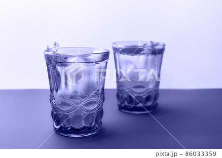 Two beautiful vintage glasses with cold drink and ice cubes, with fresh mint leaves toned in trendy color of year 2022. Backdrop with copy space for your design. Two beautiful vintage glasses with cold drink and ice cubes, with fresh mint leaves toned in trendy color of year 2022. Backdrop with copy space for your design. 86033359