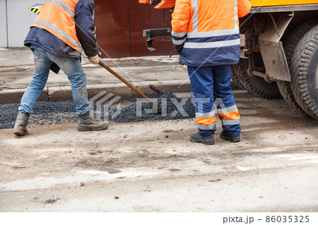 Road service workers level fresh asphalt with a shovel for patching the road. Road service workers level fresh asphalt with a shovel for patching the road. 86035325