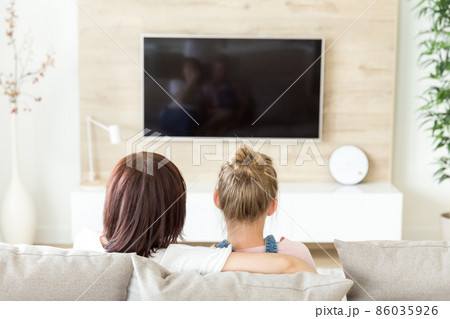 Mother and daughter sitting on sofa and watching tv, single mother concept, back view Mother and daughter sitting on sofa and watching tv, single mother concept, back view 86035926