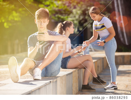 Teenager is passionate about playing on a smartphone on street 86038293