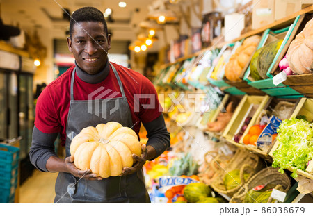 Cheerful greengrocery owner with pumpkin in hands 86038679