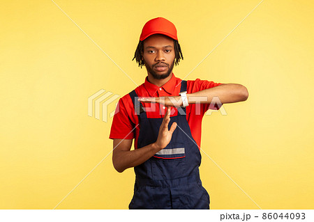 Serious worker wearing uniform, showing time out gesture, need break, working in service industry, courier delivery, housekeeping maintenance. Indoor studio shot isolated on yellow background. Serious worker wearing uniform, showing time out gesture, need break, working in service industry, courier delivery, housekeeping maintenance. Indoor studio shot isolated on yellow background. 86044093