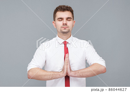 Yoga time. Portrait of young handsome calm man in white shirt and tie standing in yoga pose and try to relaxing. indoor isolated on gray background. 86044627