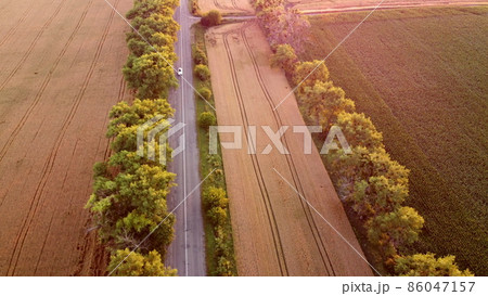 Drone flying over road between wheat fields during dawn sunset. Drone flying over road between wheat fields during dawn sunset. 86047157