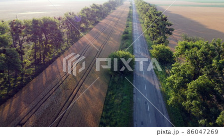 Aerial drone view flight over highway wheat field and green trees at sunset dawn 86047269