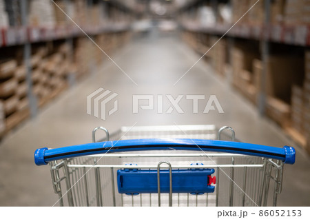 Empty shopping cart in a furniture store warehouse. Supermarket shopping basket aisle with box shelf abstract blur defocused background Empty shopping cart in a furniture store warehouse. Supermarket shopping basket aisle with box shelf abstract blur defocused background 86052153