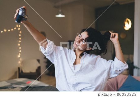 Delighted woman taking selfie on vintage camera in blurred room 86053525