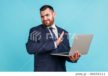 Portrait of attractive bearded young man wearing official style suit stretching hand, dont want to see, looking away, disgusting content, Indoor studio shot isolated on blue background. Portrait of attractive bearded young man wearing official style suit stretching hand, dont want to see, looking away, disgusting content, Indoor studio shot isolated on blue background. 86056311