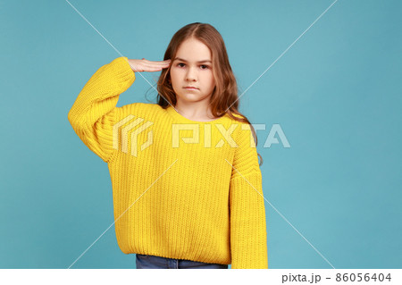 Yes, sir. Portrait of little girl saluting and looking at camera with respect, patriotic child, wearing yellow casual style sweater. Indoor studio shot isolated on blue background. Yes, sir. Portrait of little girl saluting and looking at camera with respect, patriotic child, wearing yellow casual style sweater. Indoor studio shot isolated on blue background. 86056404