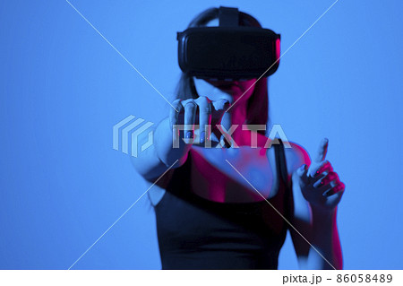 Young woman wearing VR goggles and interacts with cyberspace using swipe and stretching gestures while playing a video game with a friends in metaverse. 86058489