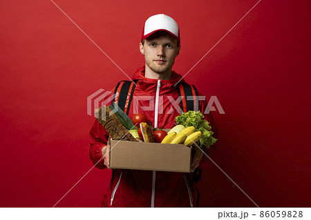 Smart food delivery service man in red uniform handing fresh food in a paper box to recipient. Express delivery, food delivery, online shopping concept. 86059828