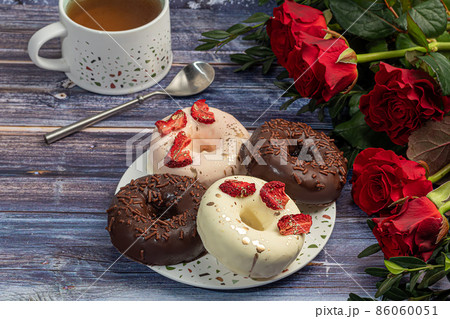 Handmade donuts on a light background in white and black chocolate. There are flowers nearby. Women's day, Valentine's day. 86060051