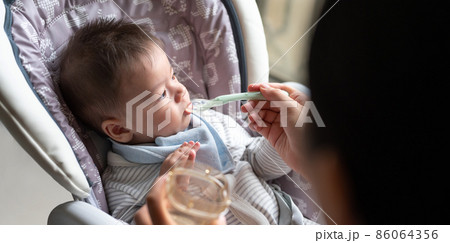 Baby boy being fed water in his high chair at home 86064356