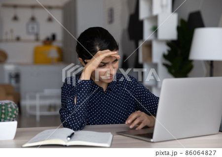 Tired upset Indian business woman working at laptop computer Tired upset Indian business woman working at laptop computer 86064827