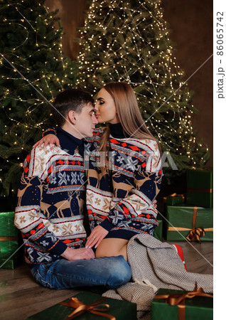 A guy and a girl hug and kiss against the background of a Christmas tree and a red sofa 86065742