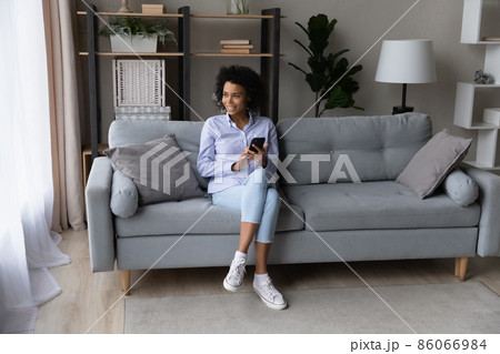 Dreamy young African woman holding smartphone in hands. 86066984