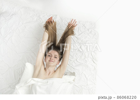 Beautiful naked caucasian woman lies in bed letting down long hair, covered with sheet and enjoys the weekend. Relaxing at home. Vertical frame 86068220
