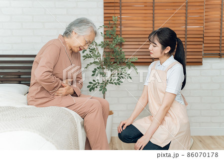 痛がる高齢者女性とエプロン姿の女性（腹痛） 86070178