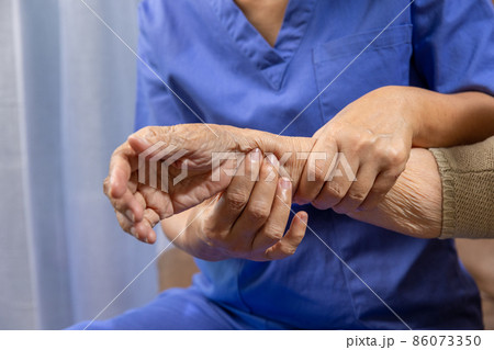 Caregiver massaging wrist of elderly woman in painful swollen gout . 86073350