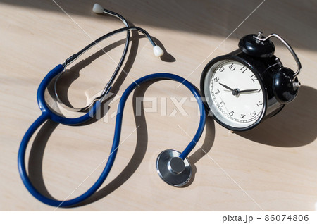 Classic old black mechanical alarm clock with stethoscope on a wooden table. Time to check the heart. Table clock and a device for measuring blood pressure. Classic old black mechanical alarm clock with stethoscope on a wooden table. Time to check the heart. Table clock and a device for measuring blood pressure. 86074806
