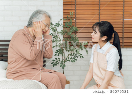 痛がる高齢者女性とエプロン姿の女性(頭痛) 痛がる高齢者女性とエプロン姿の女性(頭痛) 86079581