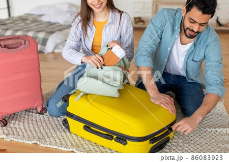 Young spouses packing clothes in suitcase and woman putting passport with tickets in bag, preparing for vacation 86083923