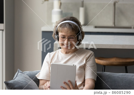 Happy old woman in headphones using digital computer tablet. 86085290