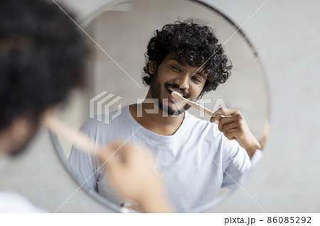 Toothcare routine concept. Young indian guy cleaning teeth in the morning using toothbrush and toothpaste 86085292