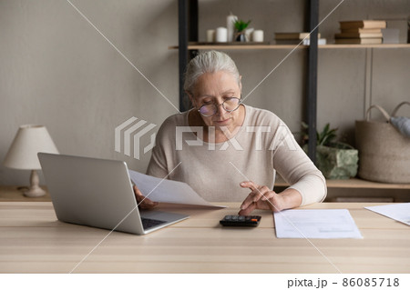 Concentrated old woman calculating utility bills at home. 86085718