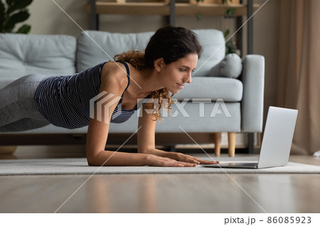 Concentrated young sporty woman working out online at home. Concentrated young sporty woman working out online at home. 86085923
