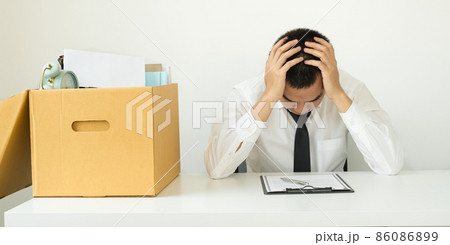 A male office worker is unhappy with being fired from a company packing things into cardboard boxes. The young man was stressed and disappointed by being fired. concept of layoffs and unemployment A male office worker is unhappy with being fired from a company packing things into cardboard boxes. The young man was stressed and disappointed by being fired. concept of layoffs and unemployment 86086899