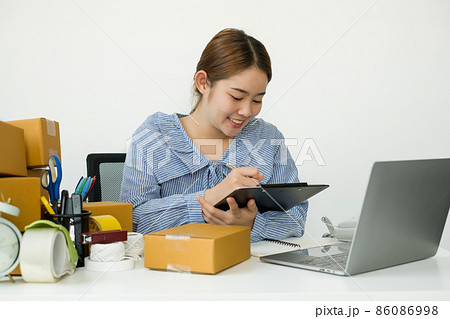 Young Asian woman business owner with many parcel boxes on the table happy online sales job, use the laptop, get an order from customers, take notes, and make arrangements for delivery by post Young Asian woman business owner with many parcel boxes on the table happy online sales job, use the laptop, get an order from customers, take notes, and make arrangements for delivery by post 86086998