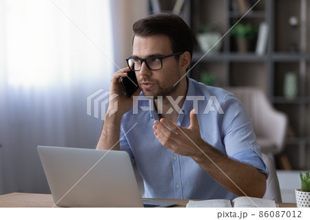 Confident businessman in glasses talking on phone, sitting at desk 86087012