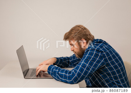 Beard emotional man in slouching position sitting in office room, working with laptop Beard emotional man in slouching position sitting in office room, working with laptop 86087189