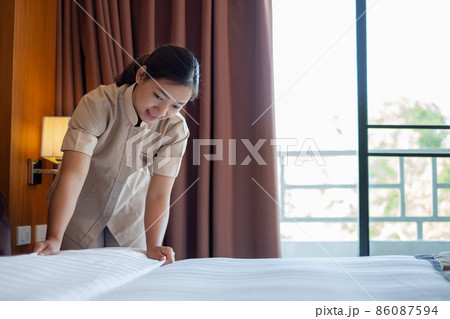 The hotel maid cleans and makes the bed in the hotel room The hotel maid cleans and makes the bed in the hotel room 86087594