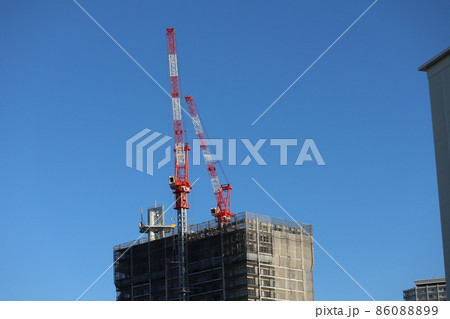真っ青な青空と1基は建材を運ぶクレーンが2基のる建築中のビルのある都会の街並みの風景 86088899