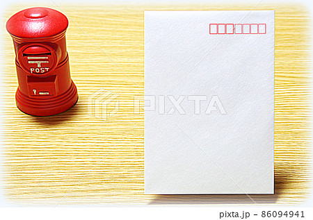 【イラスト風】木目のテーブルに置いた郵便ポスト形の貯金箱と郵便封筒（コピースペース有り） 86094941