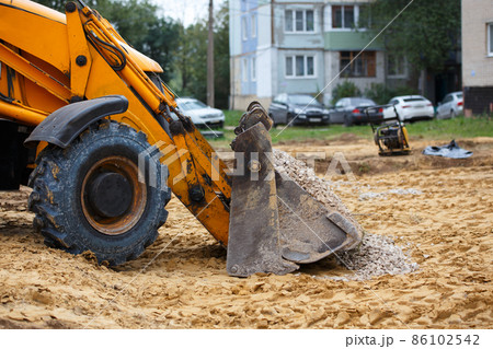 wheel bulldozer bucket filled with gravel in front of blurred cars and houses 86102542